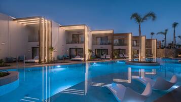 A modern hotel with a swimming pool, lounge chairs, and palm trees.