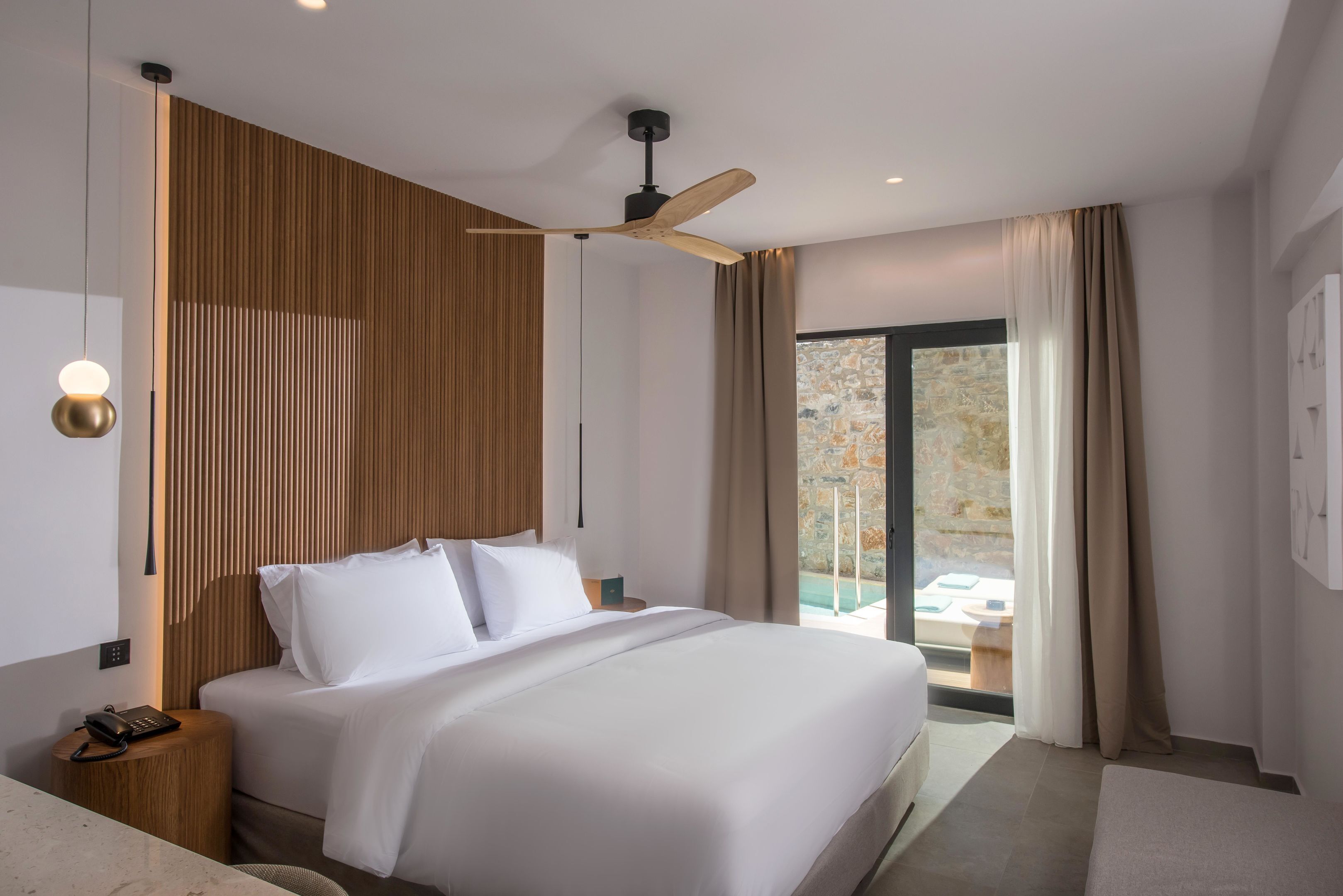 Habitación de hotel moderna con una cama grande, un revestimiento de pared de madera, un ventilador de techo y vistas al exterior.