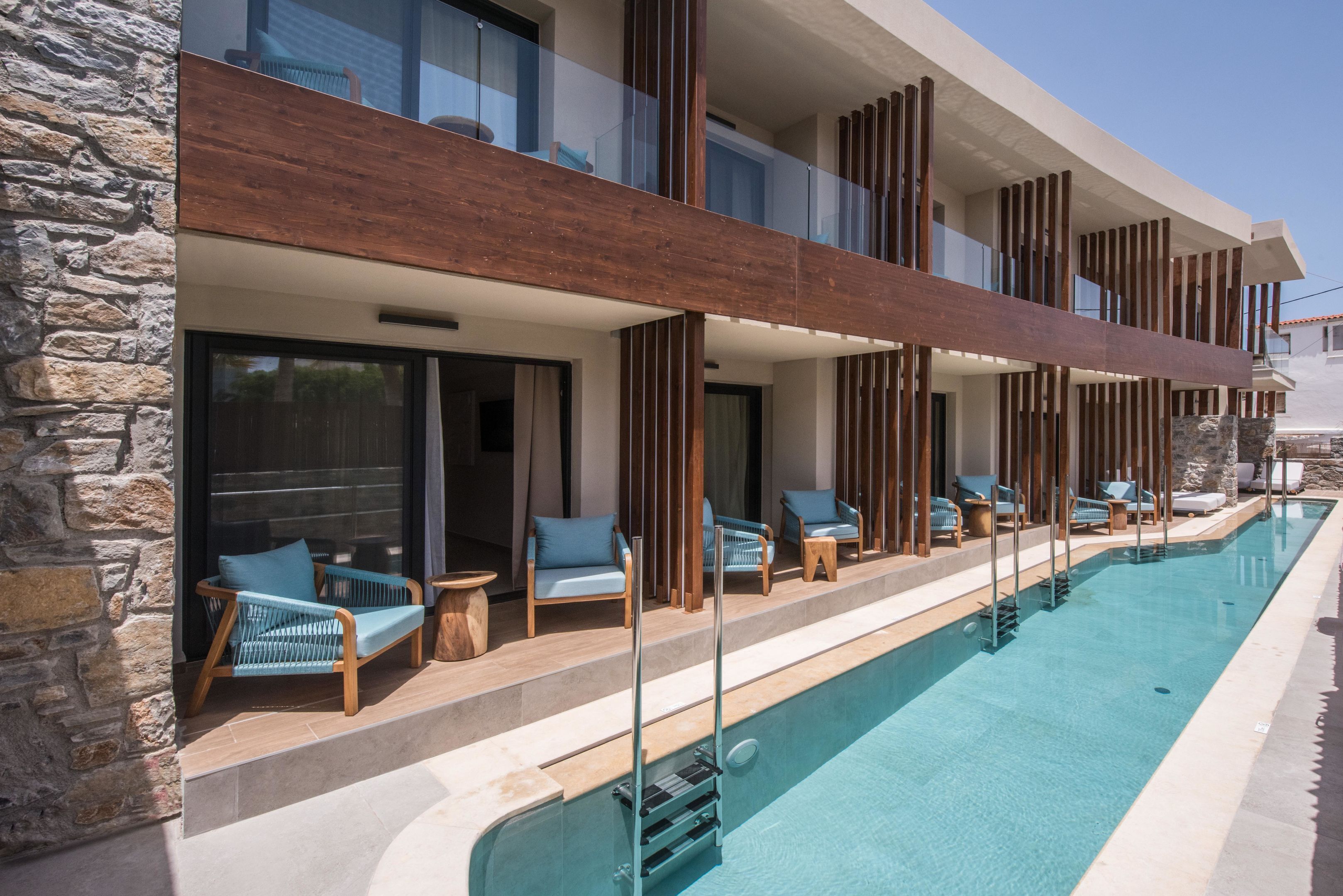 A modern hotel with a pool, stone facade, and wooden deck with lounge chairs.