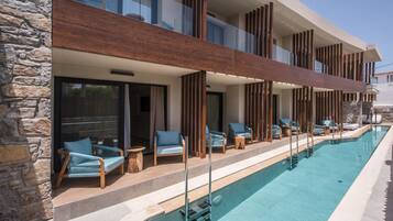 A modern hotel with a pool, stone facade, and wooden deck with lounge chairs.