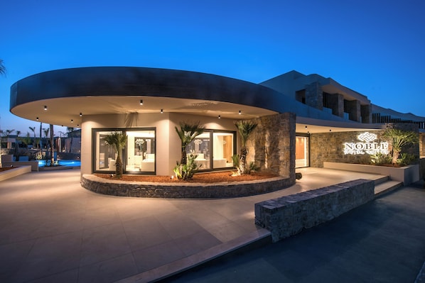 A modern hotel entrance with a curved facade, a stone wall, and a sign reading "Noble Hotel Suites".