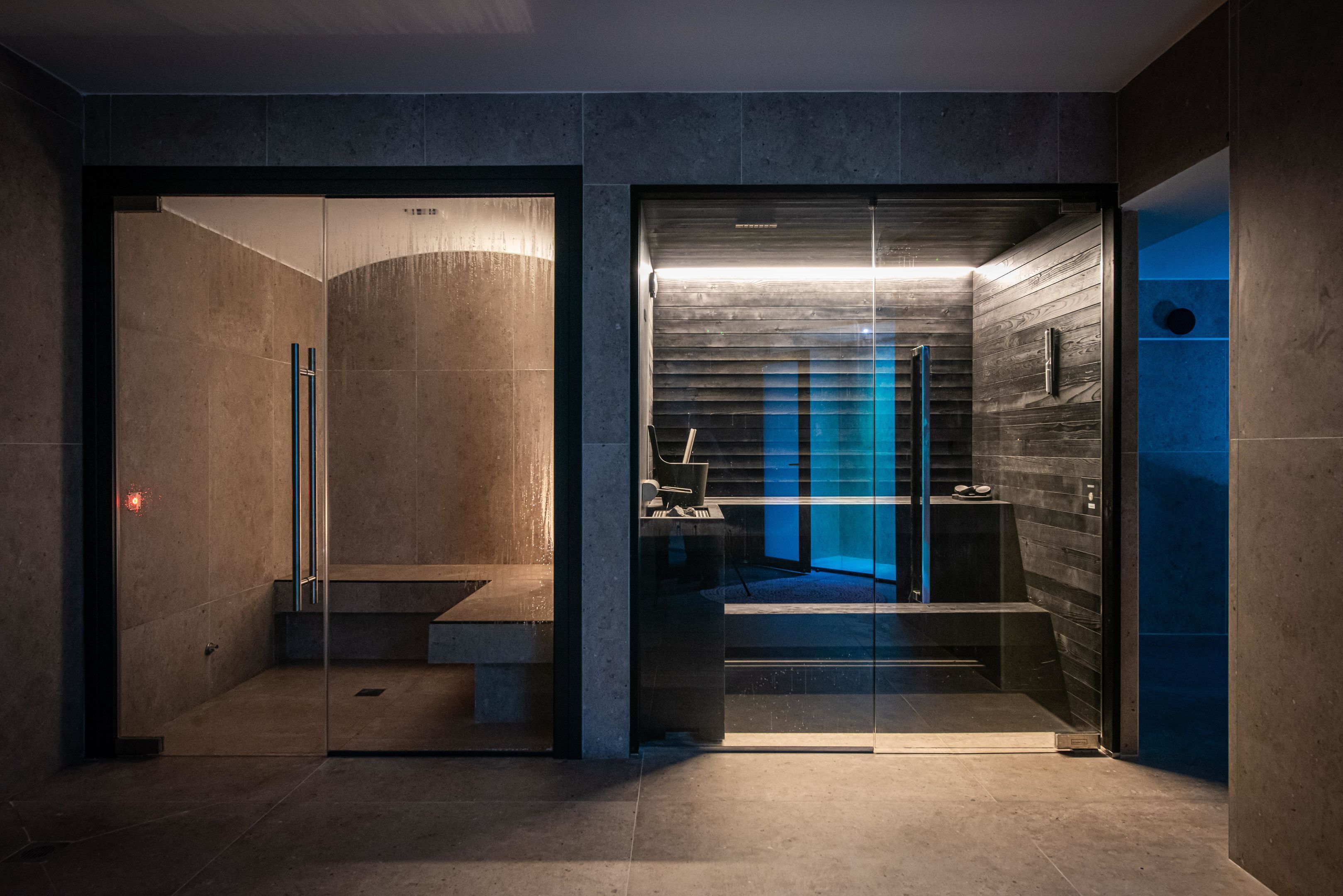 Ein modernes Badezimmer mit Glastrennwand, einem Holzkosmetikschrank und einem blau beleuchteten Duschbereich.