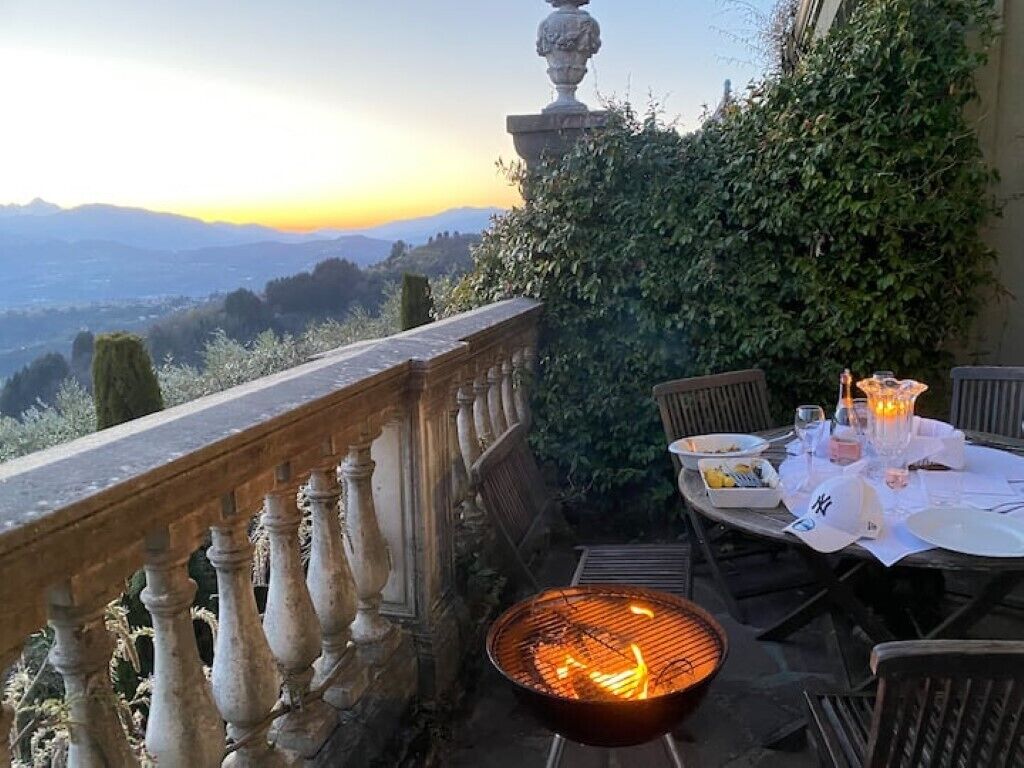An outdoor dining area with a grill, table, chairs, and a view of the landscape.