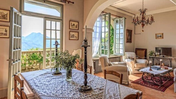 Amplia sala de estar con una gran mesa, asientos cómodos y vistas a las montañas a través de ventanas abiertas.