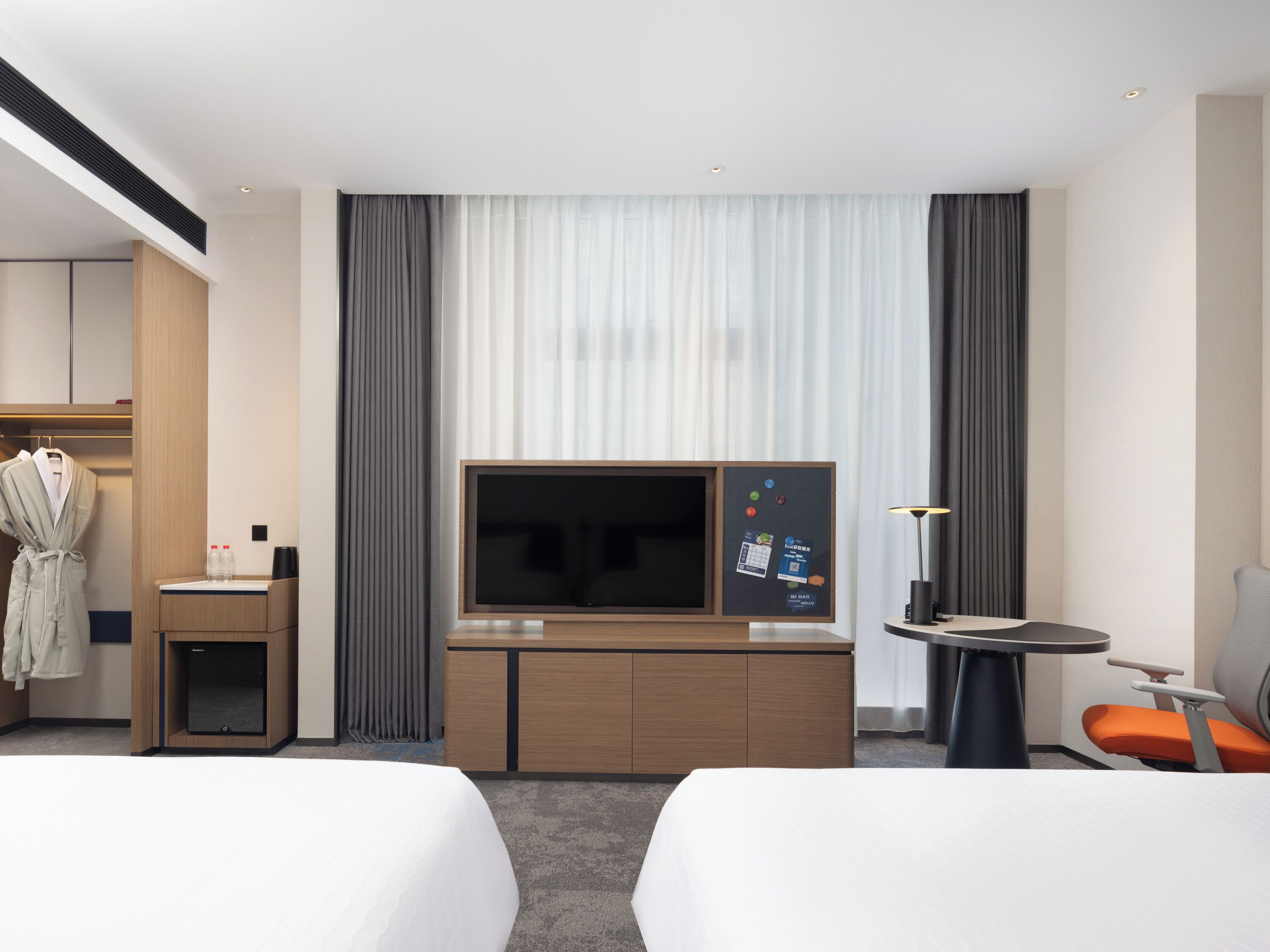 Een moderne hotelkamer met twee bedden, een televisie, een klein bureau en een stoel.