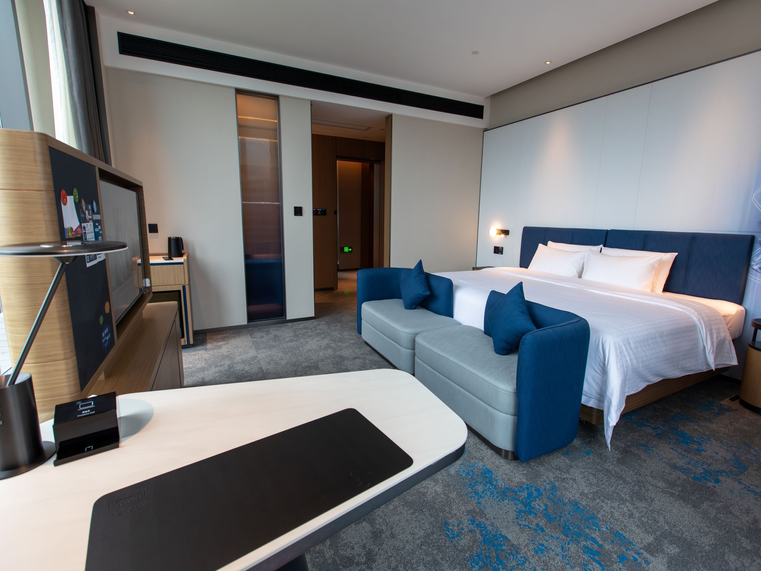 Quarto de hotel moderno com uma cama grande, um sofá, uma escrivaninha e uma televisão.
