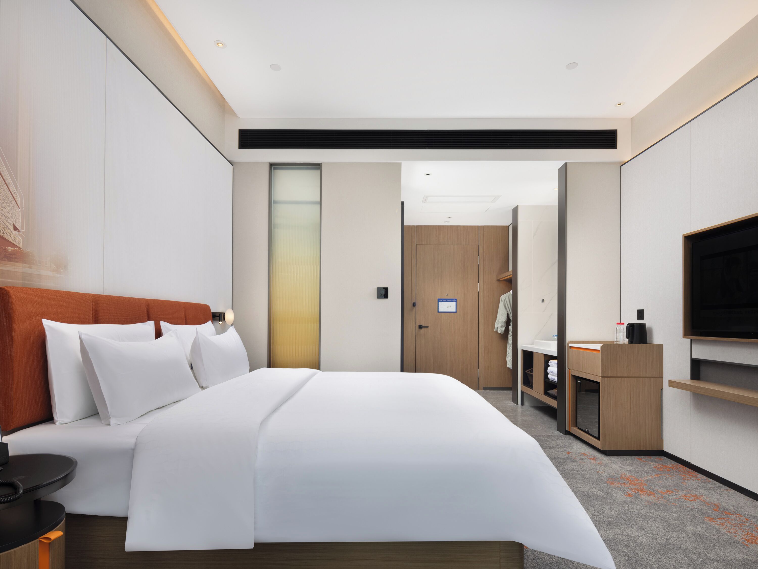 A modern hotel room with a large bed, a TV, a desk, and a wardrobe.