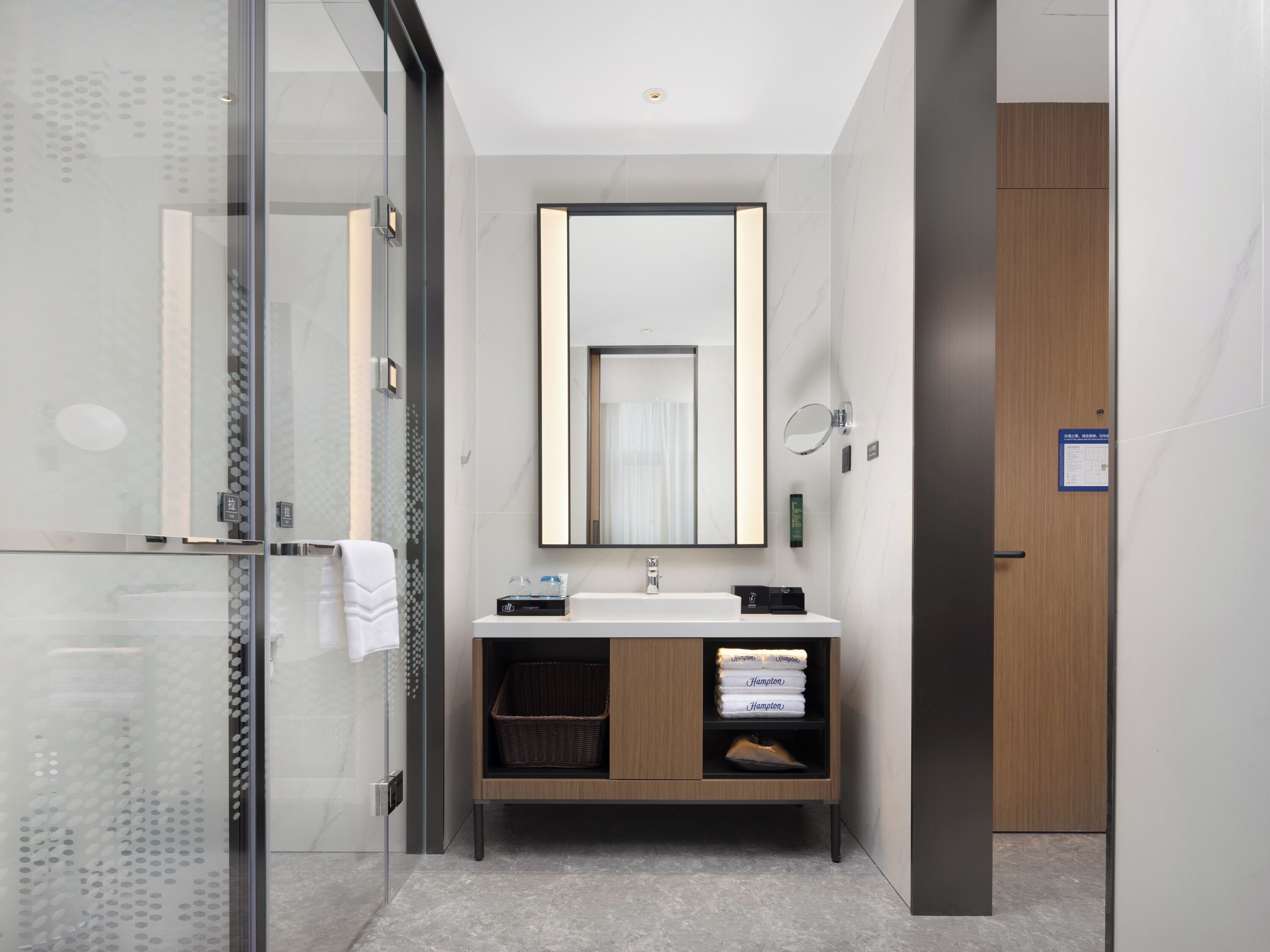 Un baño moderno con cabina de ducha de vidrio, tocador de madera con espejo y lavamanos blanco.