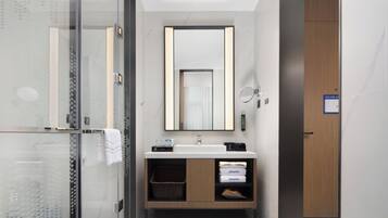 Un baño moderno con cabina de ducha de vidrio, tocador de madera con espejo y lavamanos blanco.