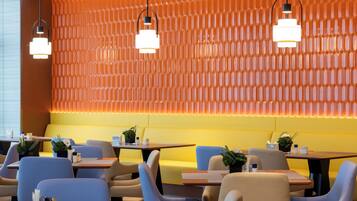 Een modern restaurantinterieur met oranje en gele zitplaatsen, blauwe stoelen en hanglampen.