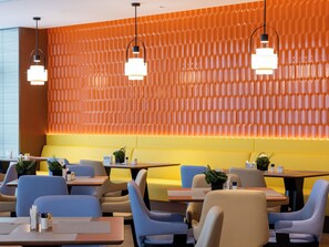 Un intérieur de restaurant moderne avec des sièges orange et jaunes, des chaises bleues et des luminaires suspendus.