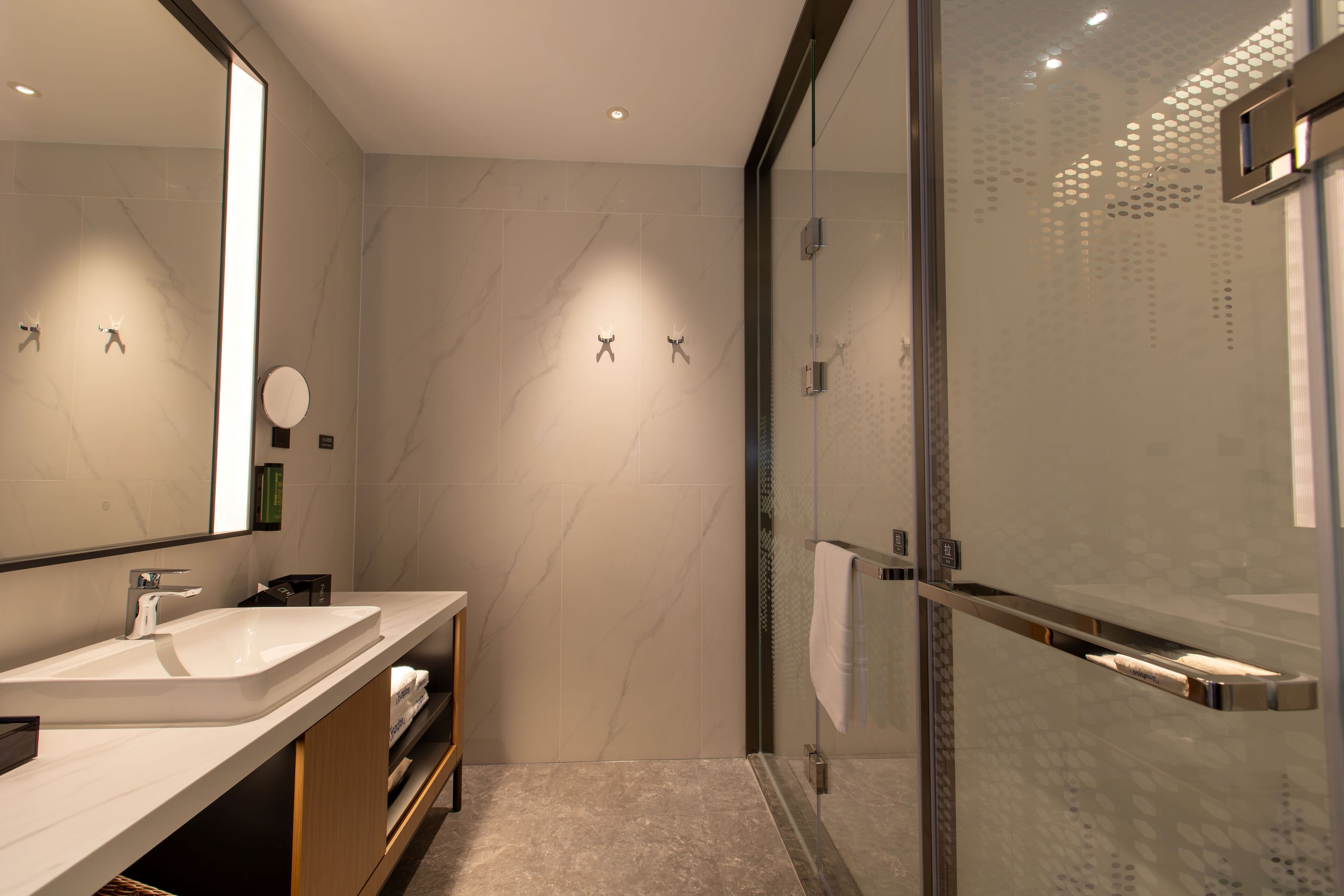 A modern bathroom with a large mirror, two sinks, a glass shower enclosure, and a towel rack.