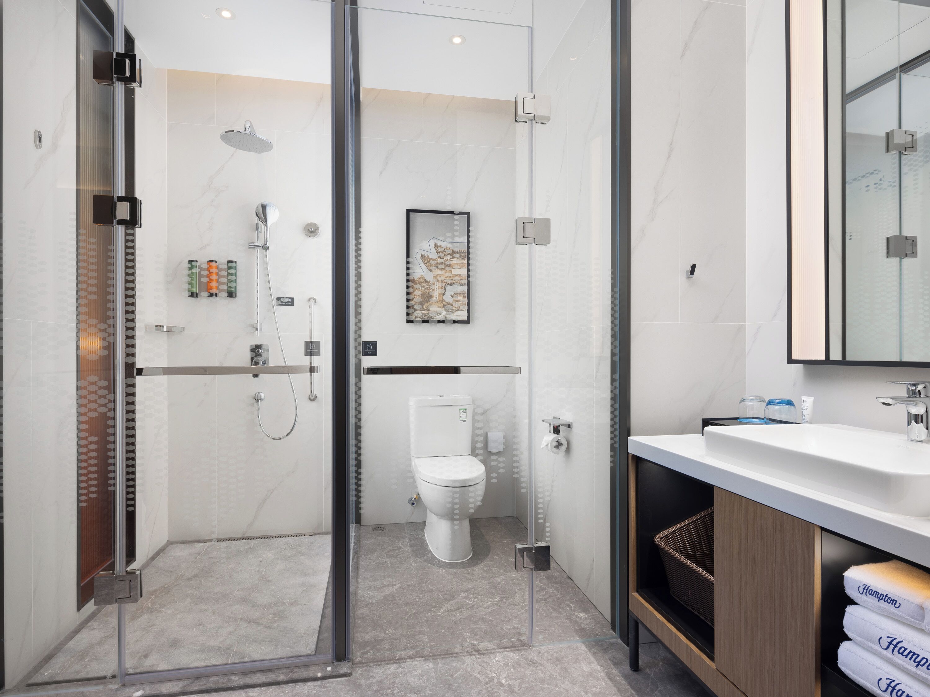 A modern bathroom with a glass-enclosed shower, a toilet, and a vanity with towels.