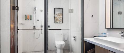 A modern bathroom with a glass-enclosed shower, a toilet, and a vanity with towels.