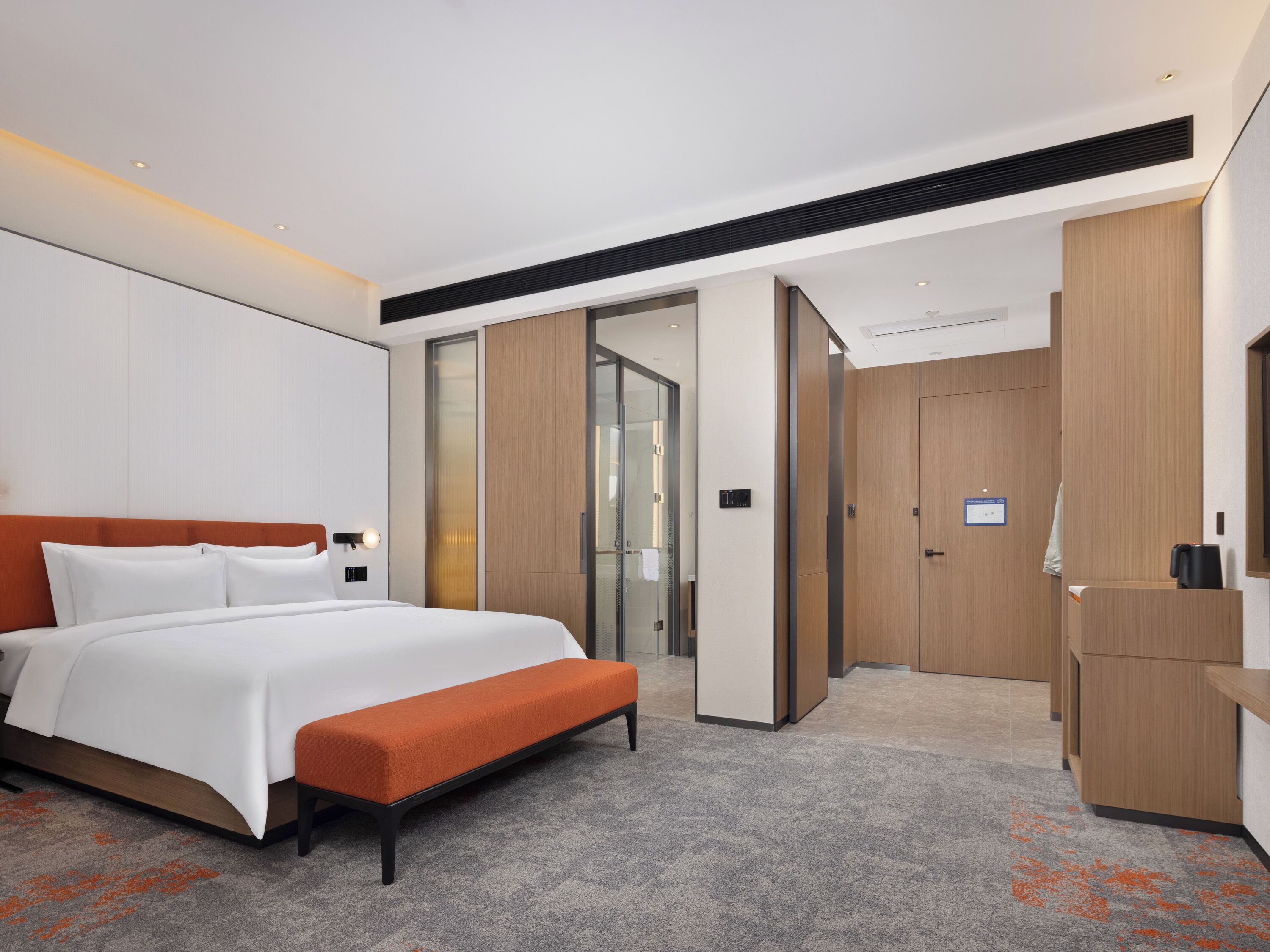 Una habitación de hotel moderna con una cama grande, un banco, un escritorio y un armario.