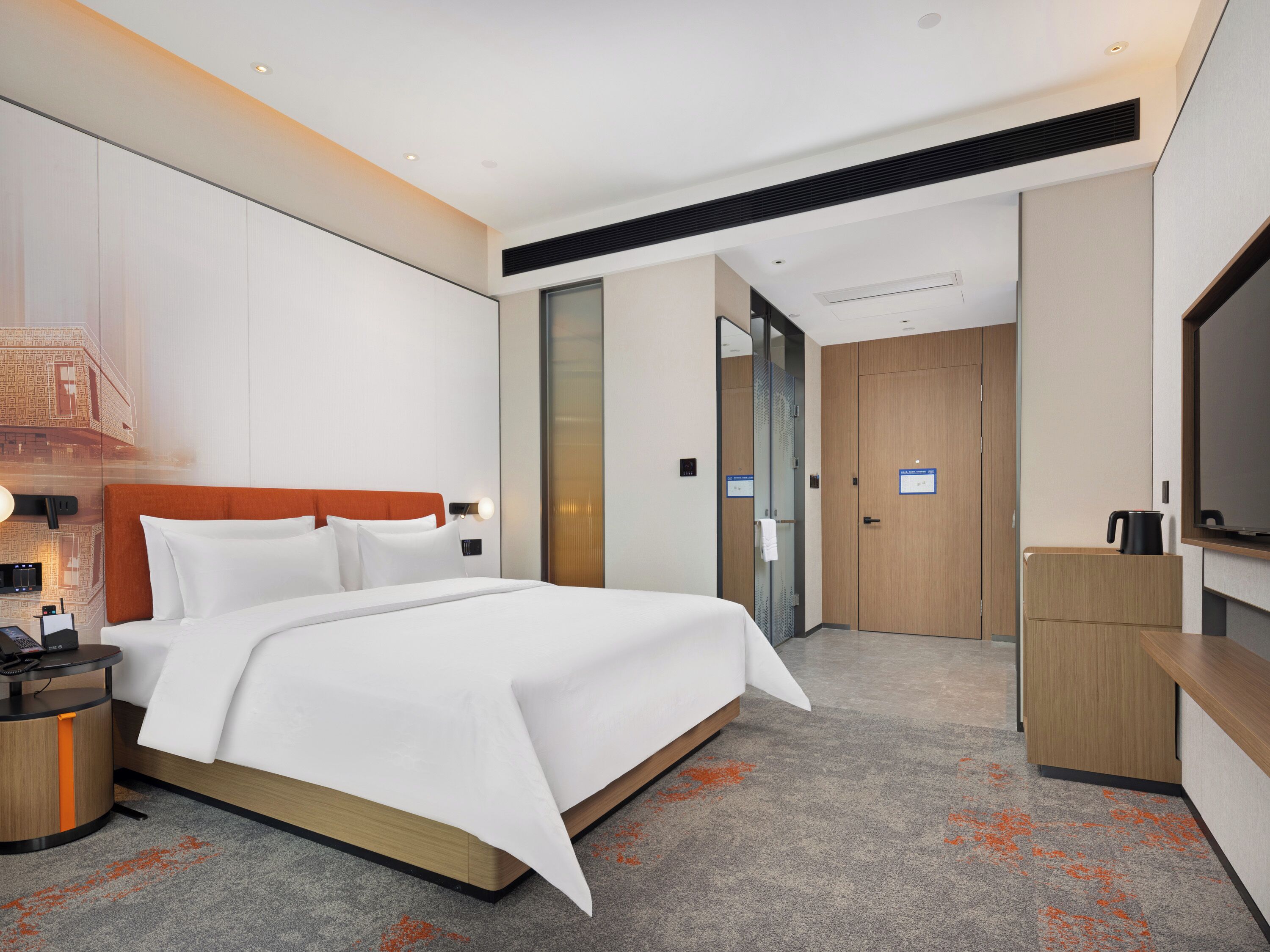 Une chambre d’hôtel moderne avec un grand lit, une table de chevet avec un téléphone et un chargeur, une télévision et une armoire.