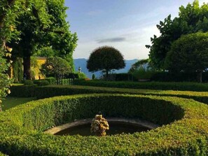 A formal garden with a central circular water feature, manicured hedges, and a large tree in the background. - Villa Paradiso,stunning views+gardens,heated pool (Coreglia Anteminelli)