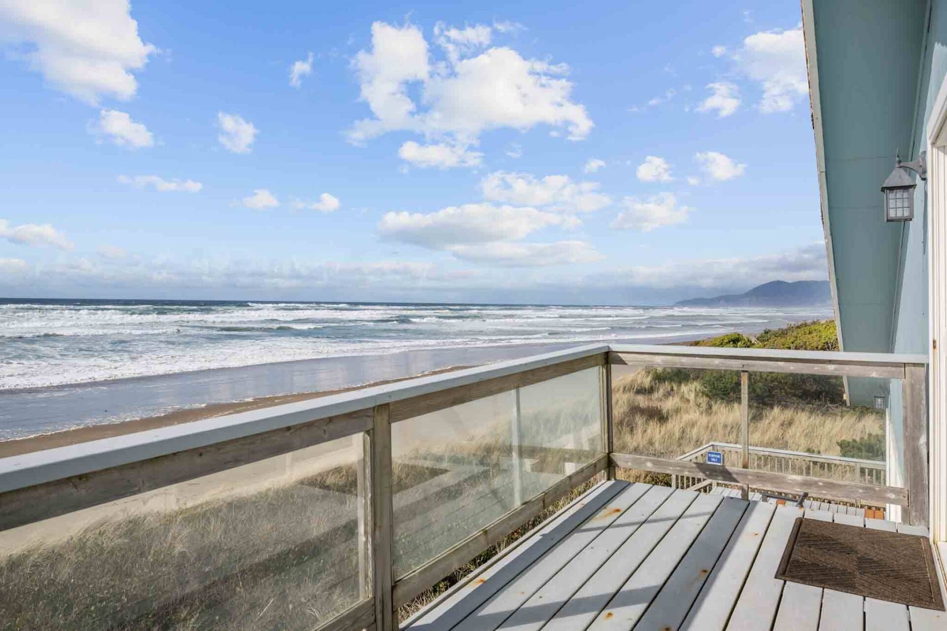 Eine Holzterrasse mit Glastrennwand, die auf einen Strand blickt.