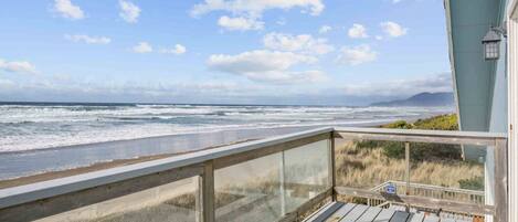 Eine Holzterrasse mit Glastrennwand, die auf einen Strand blickt.