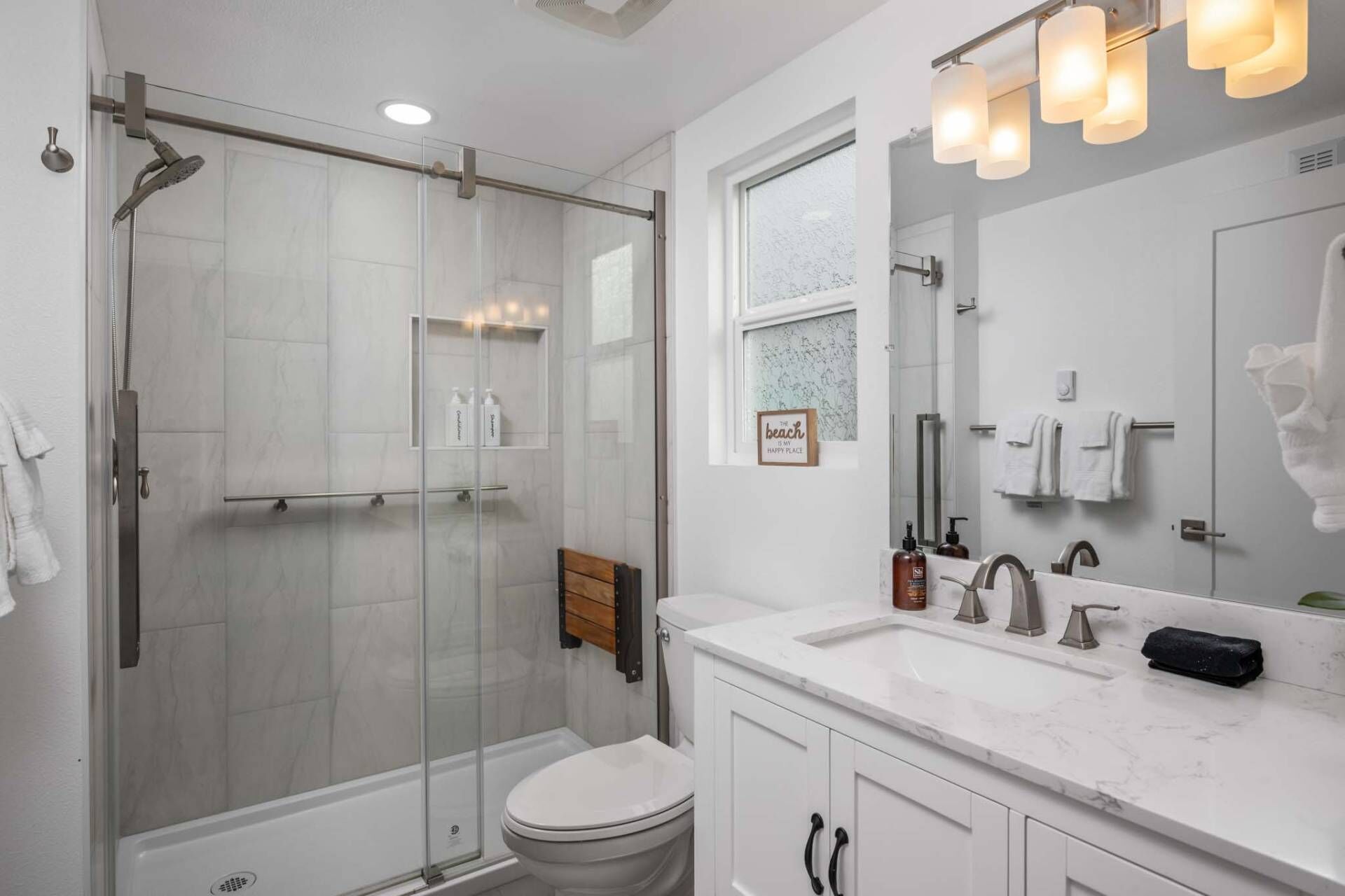 Een moderne badkamer met een douchecabine van glas, een wit toilet, een wastafel met spiegel en een raam.