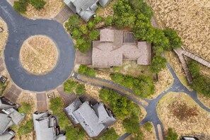 An aerial view of a residential area with a central roundabout, surrounded by houses with sloped roofs and a mix of greenery and bare ground. - Fantastic Single Level Shorepines Village Home, Steps From Beach and Ocean, 1/4 Mile to Kiwanda (Cloverdale)