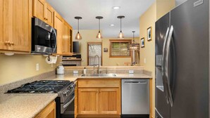 A modern kitchen with wooden cabinets, stainless steel appliances, and pendant lighting. - Fantastic Single Level Shorepines Village Home, Steps From Beach and Ocean, 1/4 Mile to Kiwanda (Cloverdale)