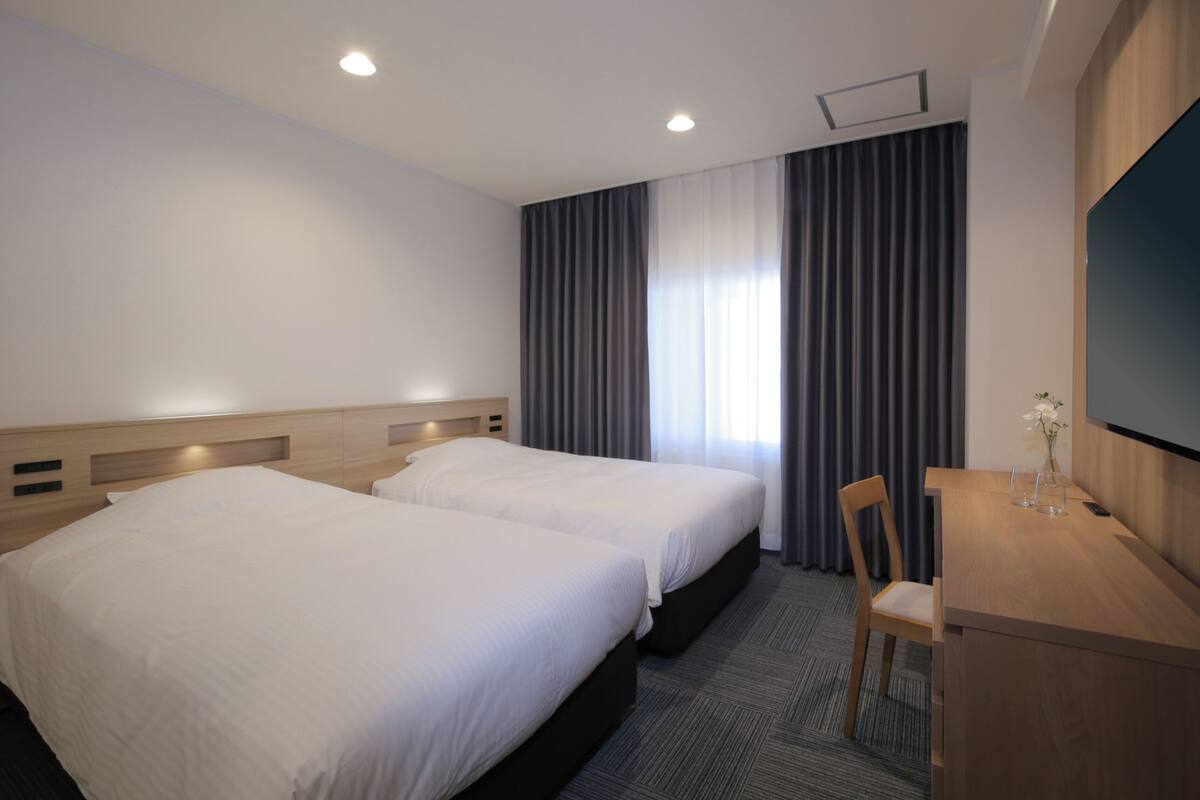 A hotel room with two beds, a desk, and a TV.