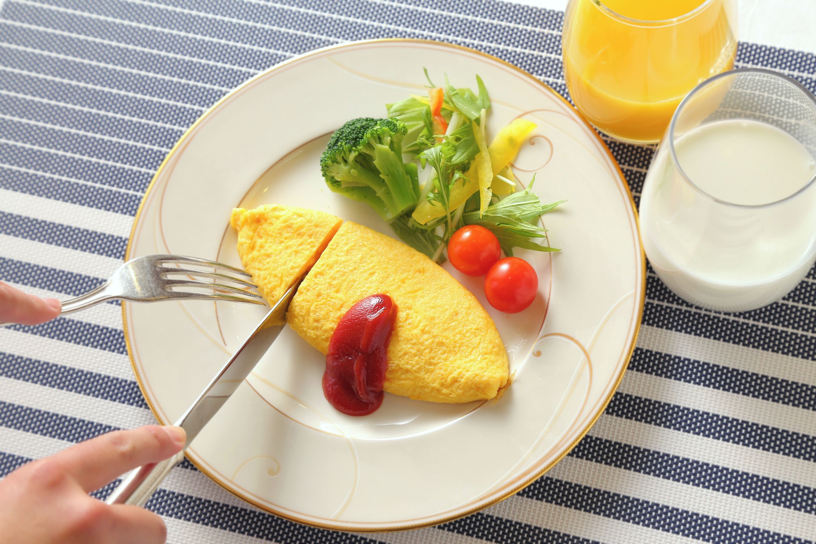 A plate with an omelette, vegetables, and a glass of orange juice on a striped tablecloth.