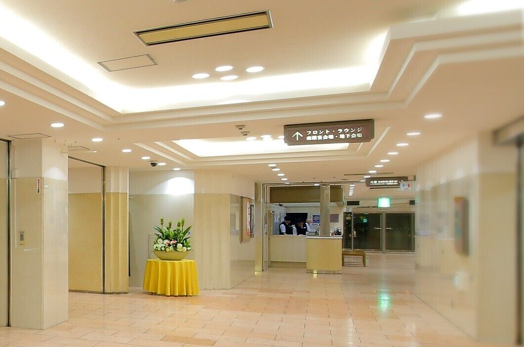 A hotel lobby with a reception desk, a yellow table with flowers, and directional signs.