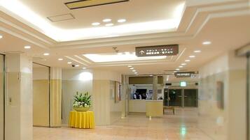 A hotel lobby with a reception desk, a yellow table with flowers, and directional signs.