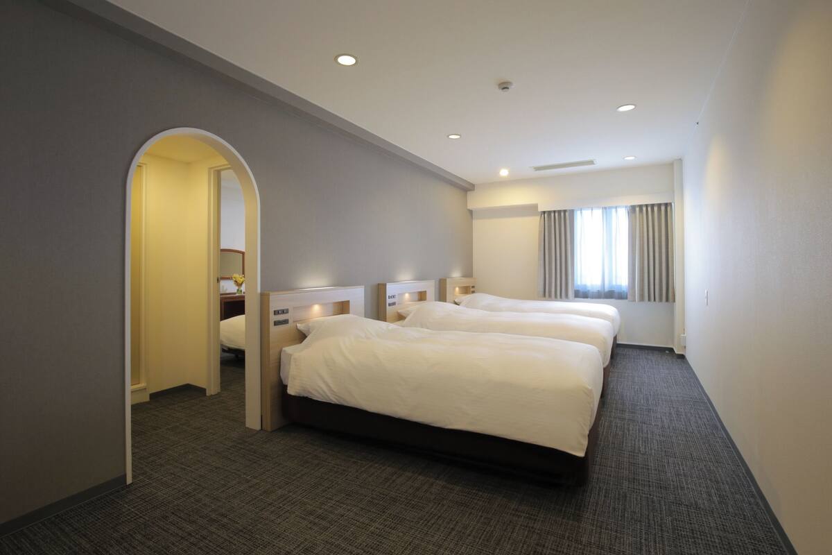 A hotel room with two beds, a mirror, a small table with a vase, and a window with curtains.
