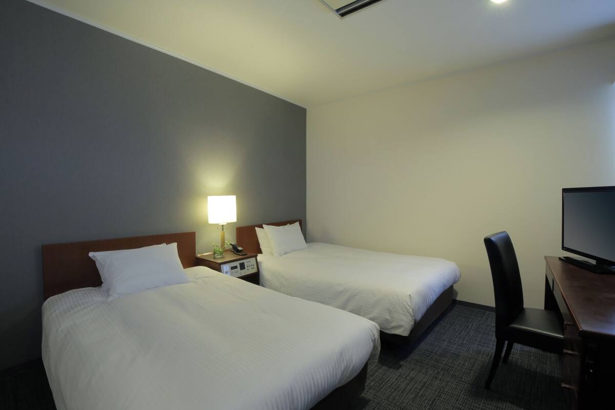 A hotel room with two beds, a desk with a television, and a chair.