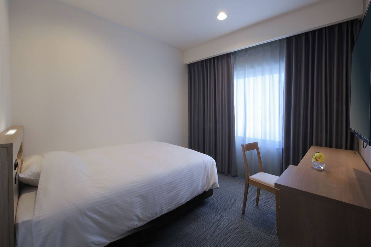 A hotel room with a large bed, a wooden desk, a chair, and a television.