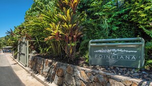 Une enseigne indiquant « Poinciana Lodge », avec un mur en pierre et des plantes tropicales.