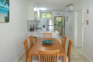 A compact kitchen with a dining area, a refrigerator, a sink, and a window with blinds.