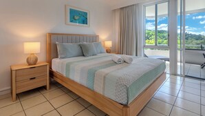 Une chambre à coucher comprenant un lit, deux tables de chevet, une commode, une fenêtre avec des rideaux et une vue sur la verdure.