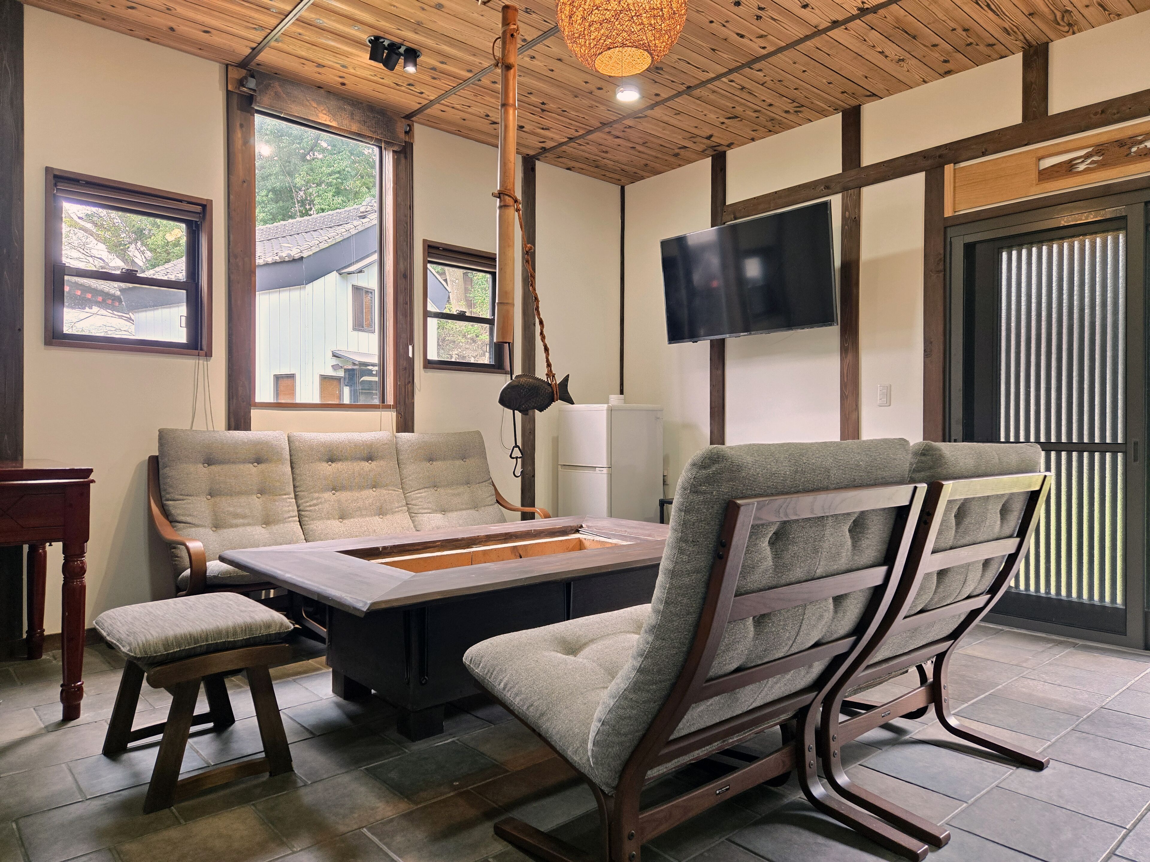 A modern living room with a wooden ceiling, large windows, a flat-screen TV, and a dining table.