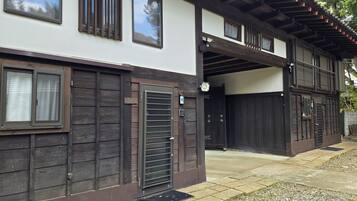 A traditional Japanese-style building with a wooden exterior, a covered entrance, and a small garden area with gravel and stepping stones.