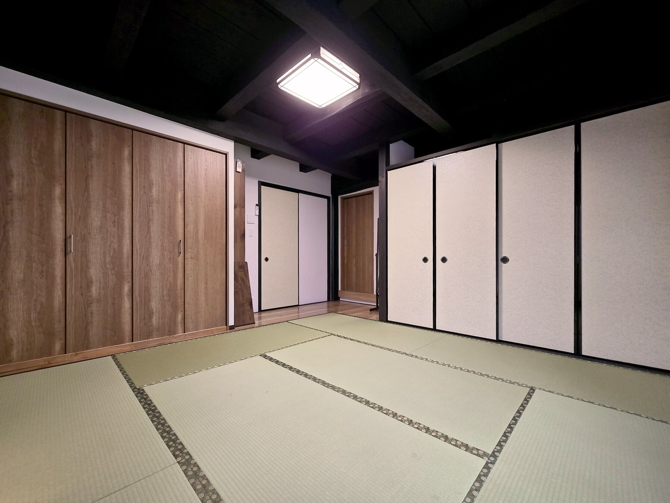 A traditional Japanese room with tatami flooring, wooden sliding doors, and a ceiling light fixture.