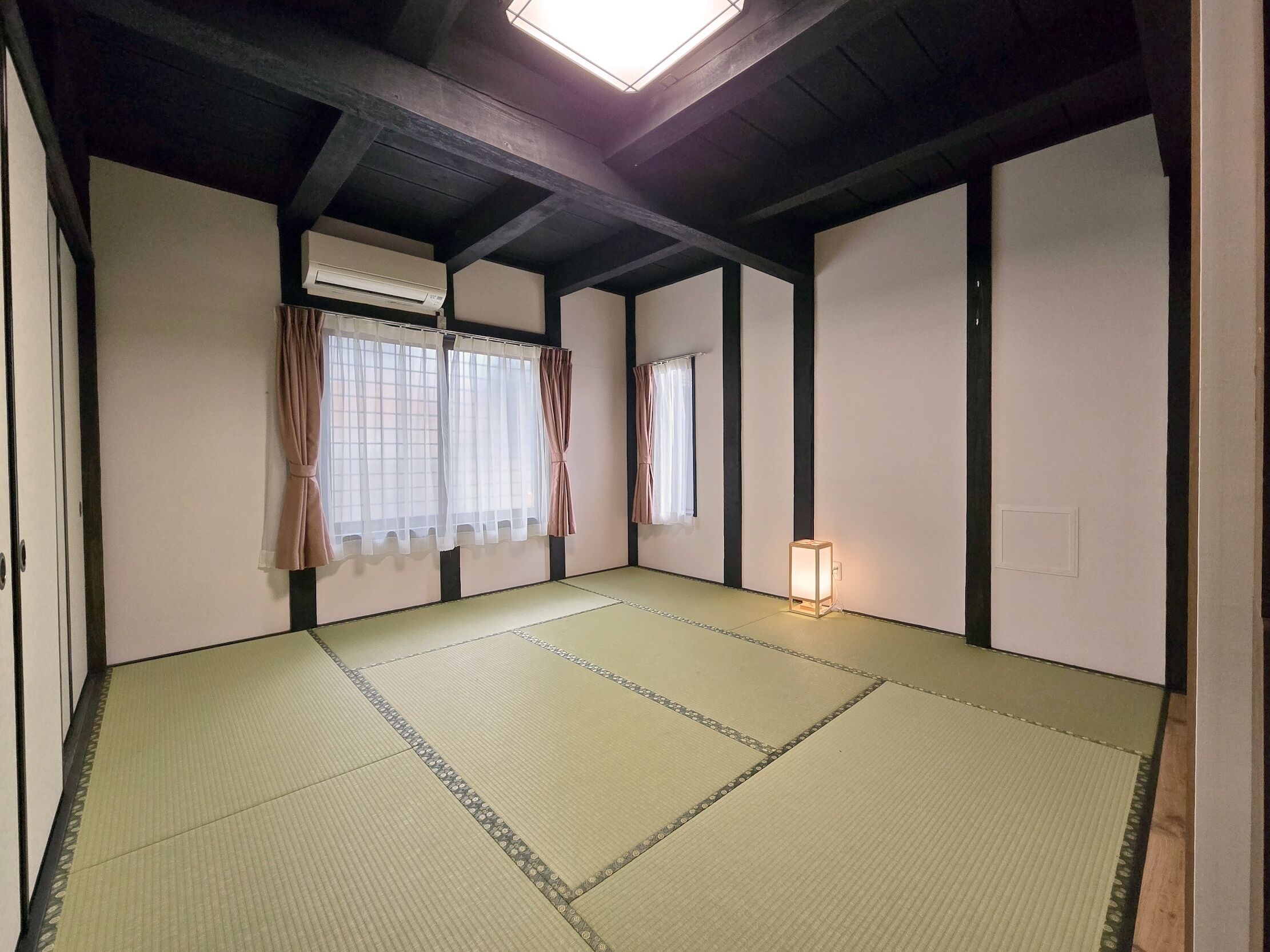 A tatami mat room with a ceiling fan, air conditioning unit, and a small table with a lamp.