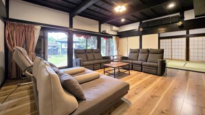 A spacious living room with a wooden floor, a sofa, a coffee table, and a view of a traditional Japanese garden through large windows. - One Night One View One Destiny (Yotsukaido)