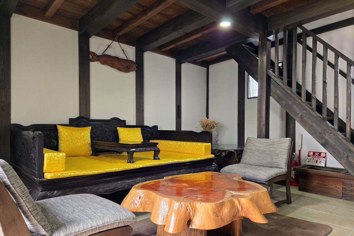 Un saló tranquil amb un sofà de fusta, una taula de centre rodona de fusta i un butac armchair gris.