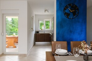 A dining area with a table set for two, a clock on the wall, and a view of the kitchen and balcony. - Villa Luka (Istria - Labin) (Labin)