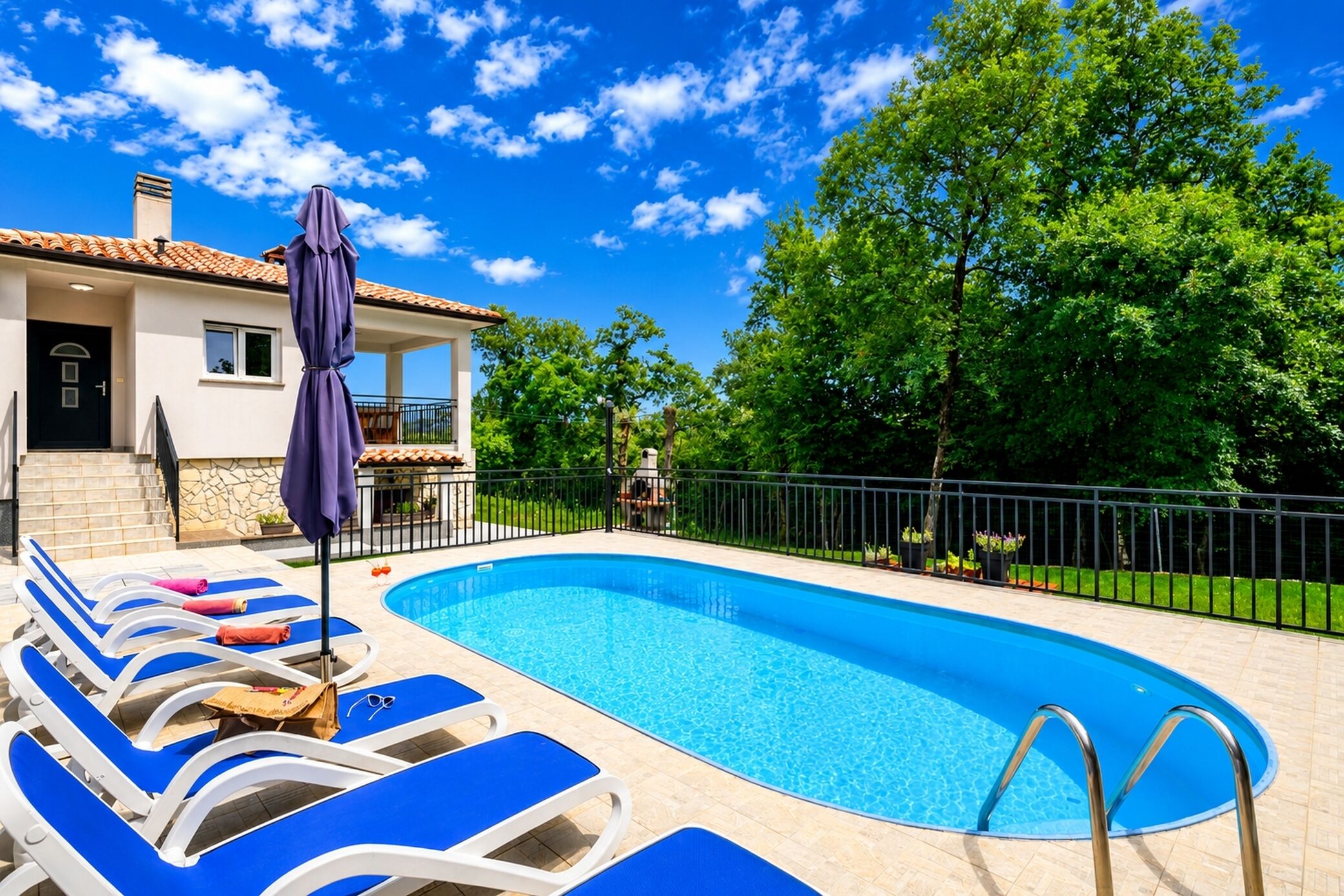 Une piscine entourée d’un jardin clos, avec des chaises longues bleues et un parasol.
