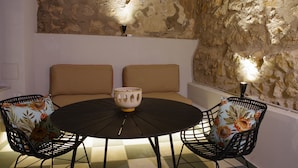 Une table ronde avec un grand bol au centre, entourée de quatre chaises dotées de coussins à motifs floraux, le tout placé devant un mur de pierre et agrémenté de deux lampes fixées au mur.