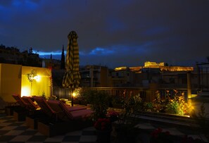 Una terraza en la azotea con sillones de descanso, un paraguas a rayas y plantas en macetas.