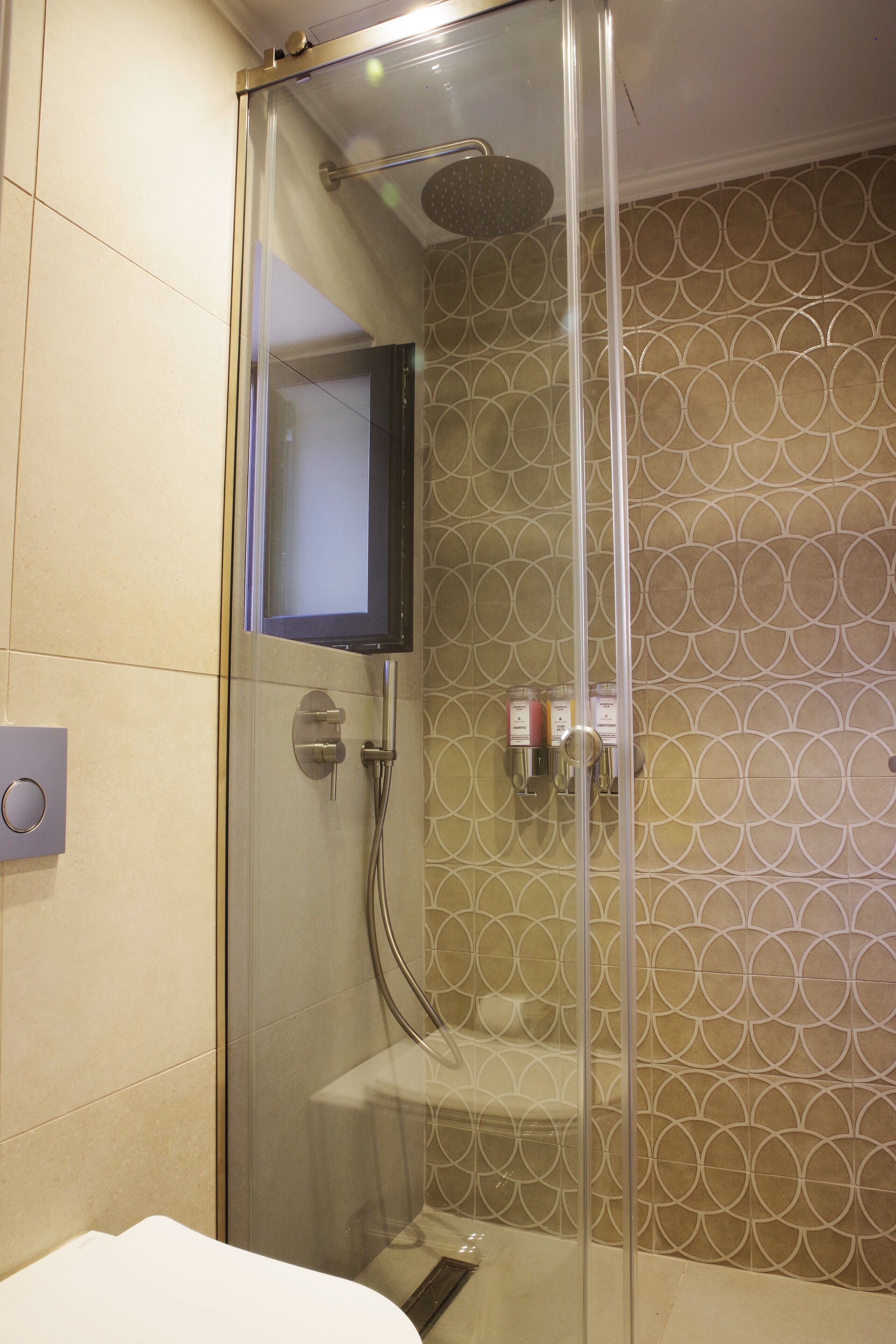 A glass-enclosed shower with a mounted television, a towel rack, and a toilet paper holder on the wall.