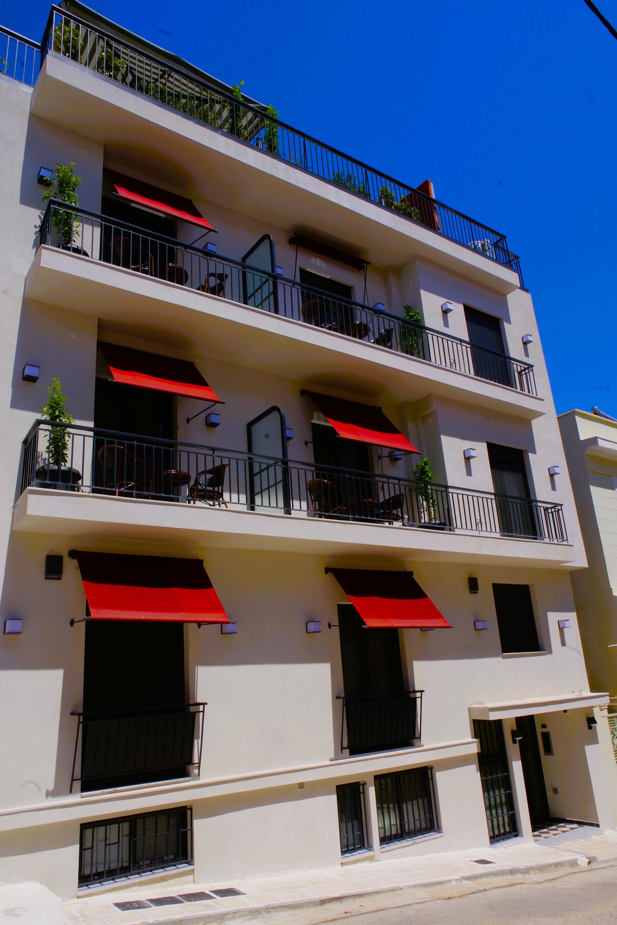 A multi-story building with balconies, red awnings, and potted plants.