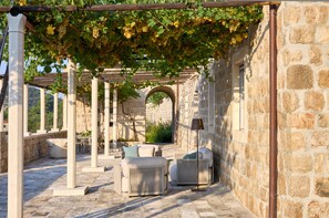 Un espacio de estar al aire libre con paredes de piedra, una pérgola cubierta de parras, columnas de piedra y un arco rústico de piedra.
