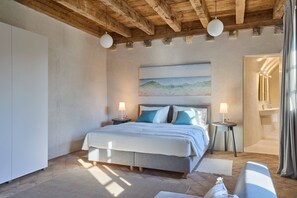 Un dormitorio con cama, mesitas de noche, un cuadro y un baño con lavabo y espejo.